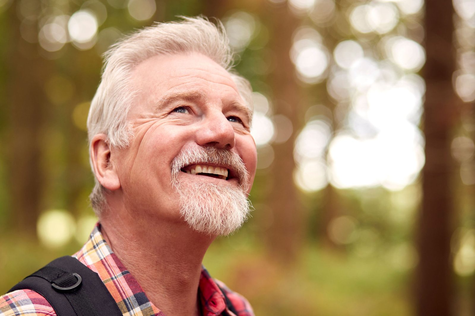 Retired man smiling and looking up during a walk through the woods